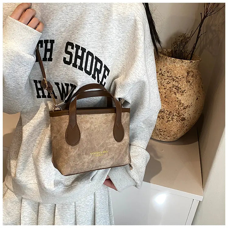 Beige canvas mini tote bag with brown leather handles and trim shown as a retro bucket bag textured canvas shoulder handbag.