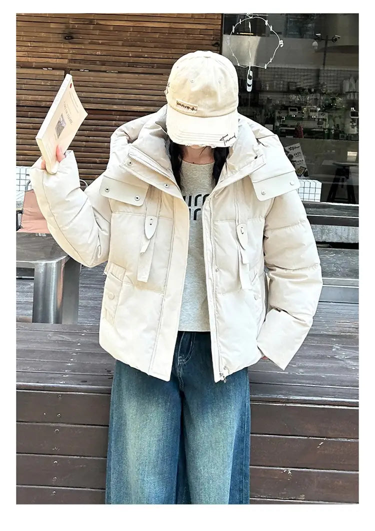 Veste courte matelassée à capuche pour femme beige, réalisée dans un matériau chaud, avec plusieurs poches à rabat et fermetures par boutons pour un usage en hiver.