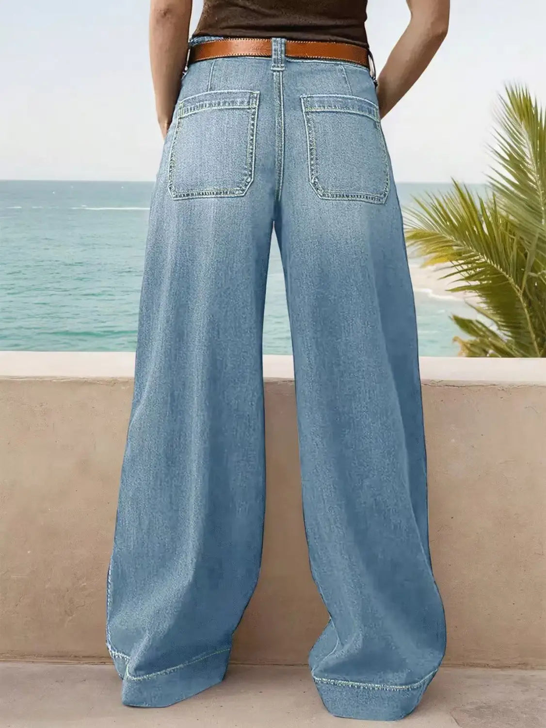wide leg denim pants in light wash with a brown leather belt shown from the front.