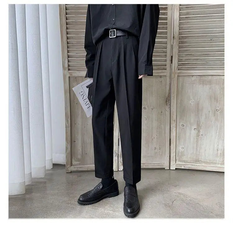 Men loose fit straight leg suit pants in black with pleated tailored fit and subtle creases paired with matching black shoes.