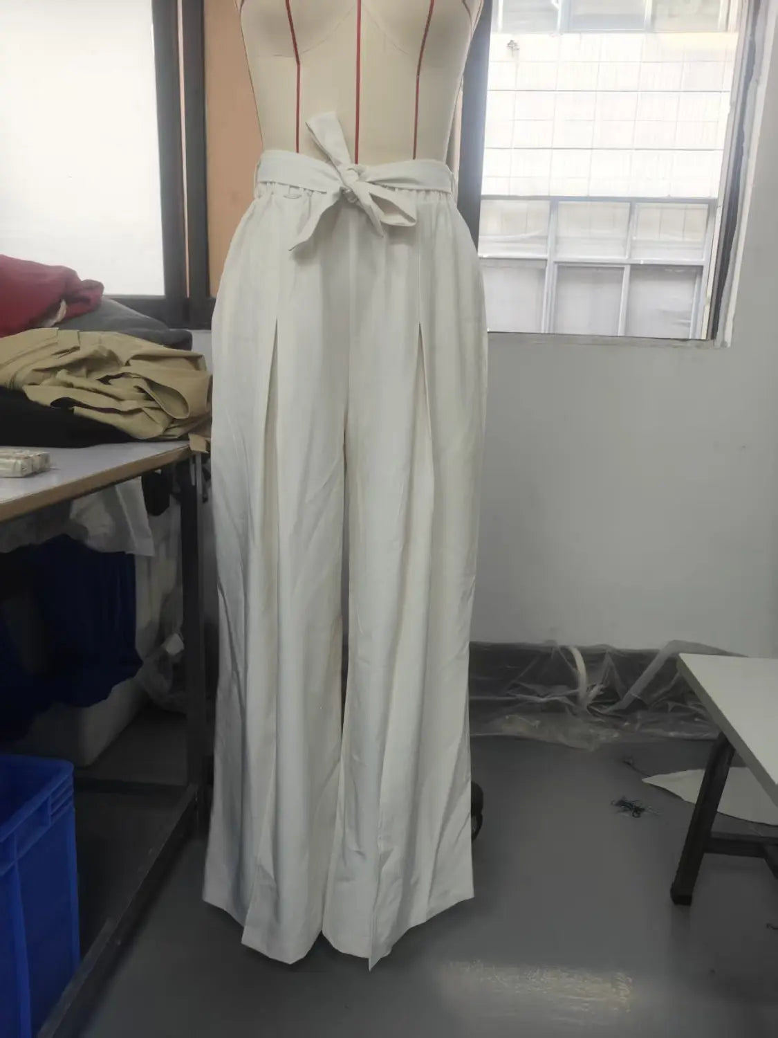 Pantalon ample à taille haute ivoire plissé, ceinture nouée, présenté sur un mannequin pour un port décontracté ample