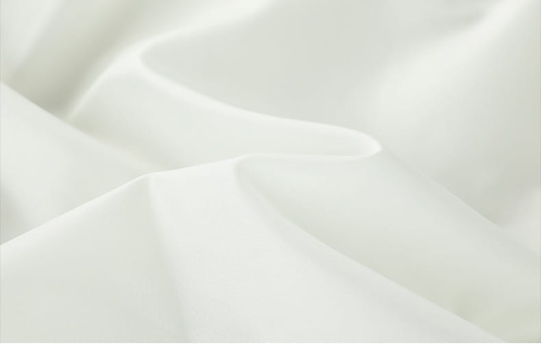 Weicher weißer Satinstoff mit sanften Falten, die die glatte, glänzende Textur einer taktischen Kapuzen-Shelljacke mit Ärmelpatch-Details hervorheben.