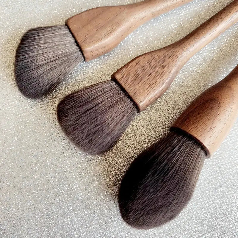 Three wooden-handled walnut wood makeup brushes with dense dark brown soft fiber bristles arranged diagonally in a makeup brush set.