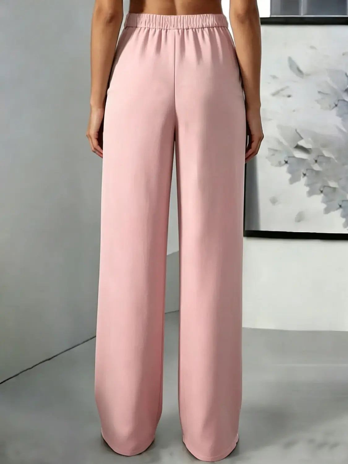 Pantalons plissés à jambes larges et taille haute rose tendre, avec une ceinture élastique réalisée dans un tissu léger.