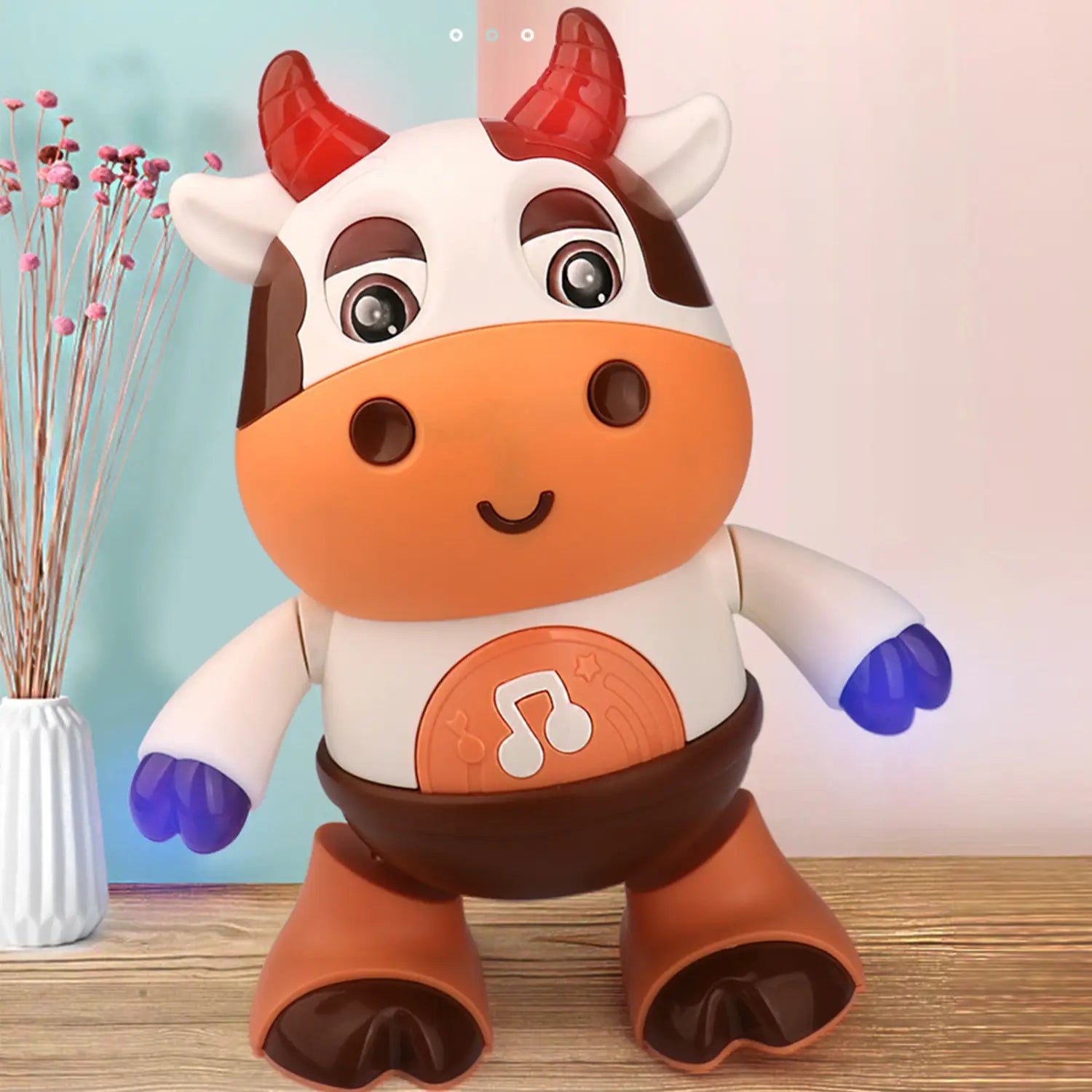 A charming orange and white plastic dancing cow musical robot toy with red horns, brown spots, blue hands, and a musical note emblem on its belly.