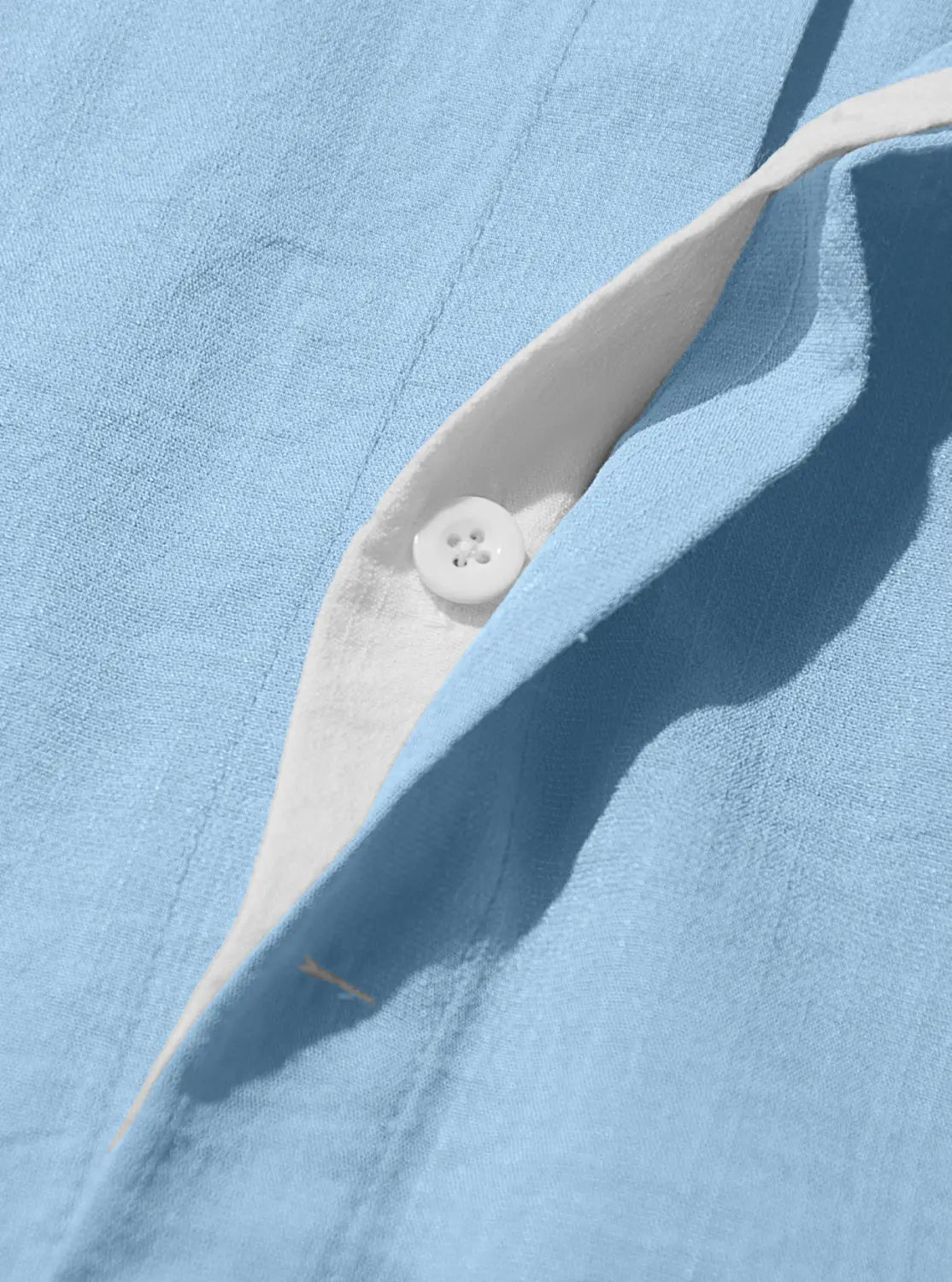 A white four-hole button nestled in the placket of a light blue men’s textured bamboo linen short sleeve button down shirt.