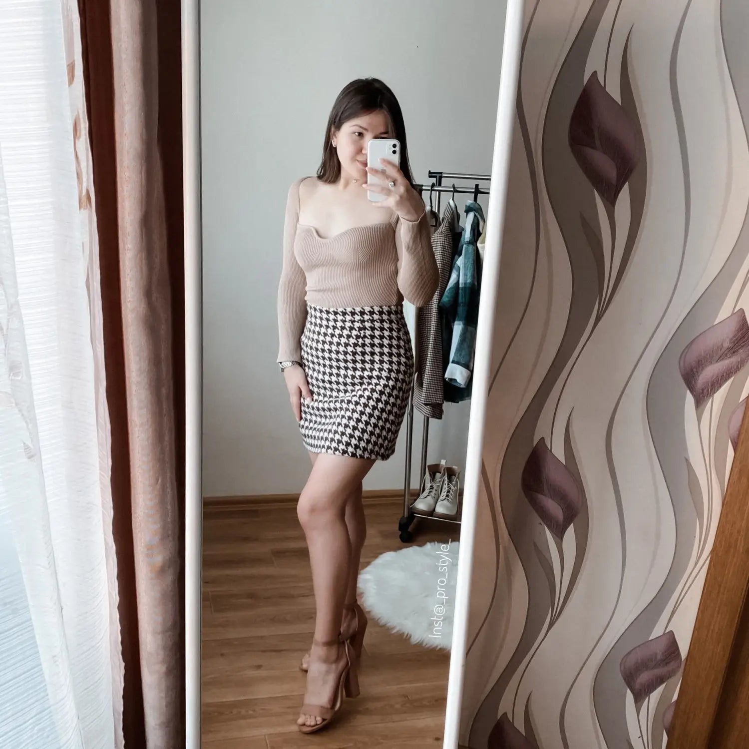 A woman wearing a beige ribbed sweetheart neck long sleeve knit pullover paired with a black and white houndstooth mini skirt.