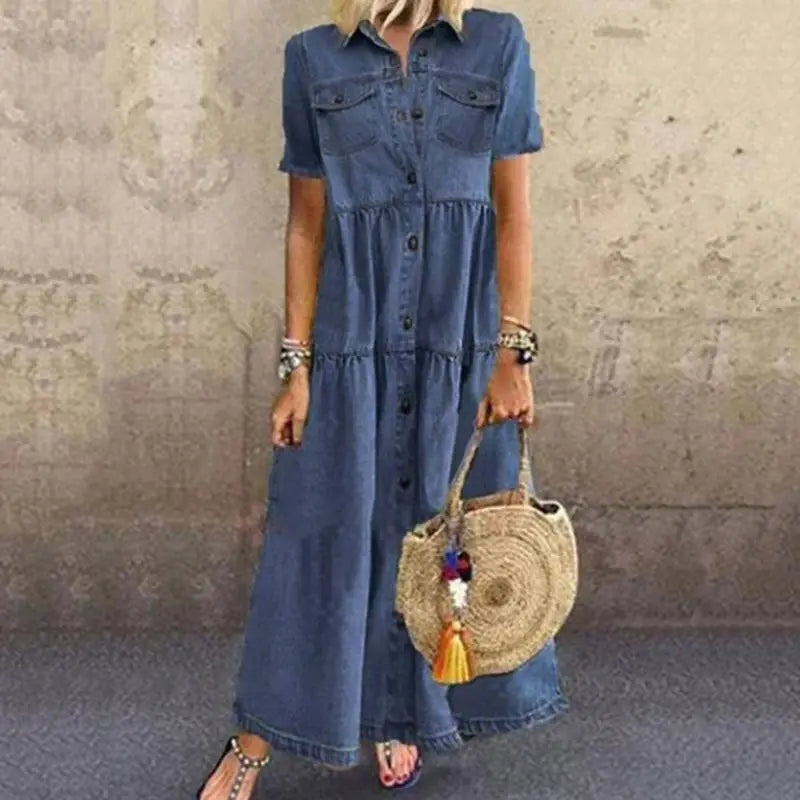 A woman wears a blue denim maxi shirt dress with short sleeves button-front closure tiered ruffles and distressed multi buckle details.