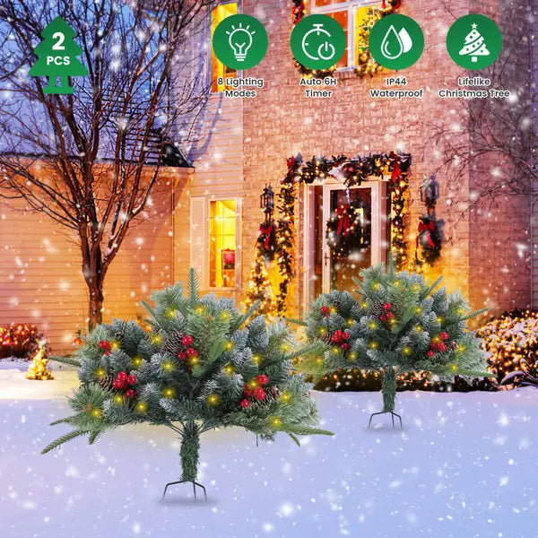 Two artificial Christmas trees with green needle-like foliage and red berries illuminated by warm yellow LED lights.