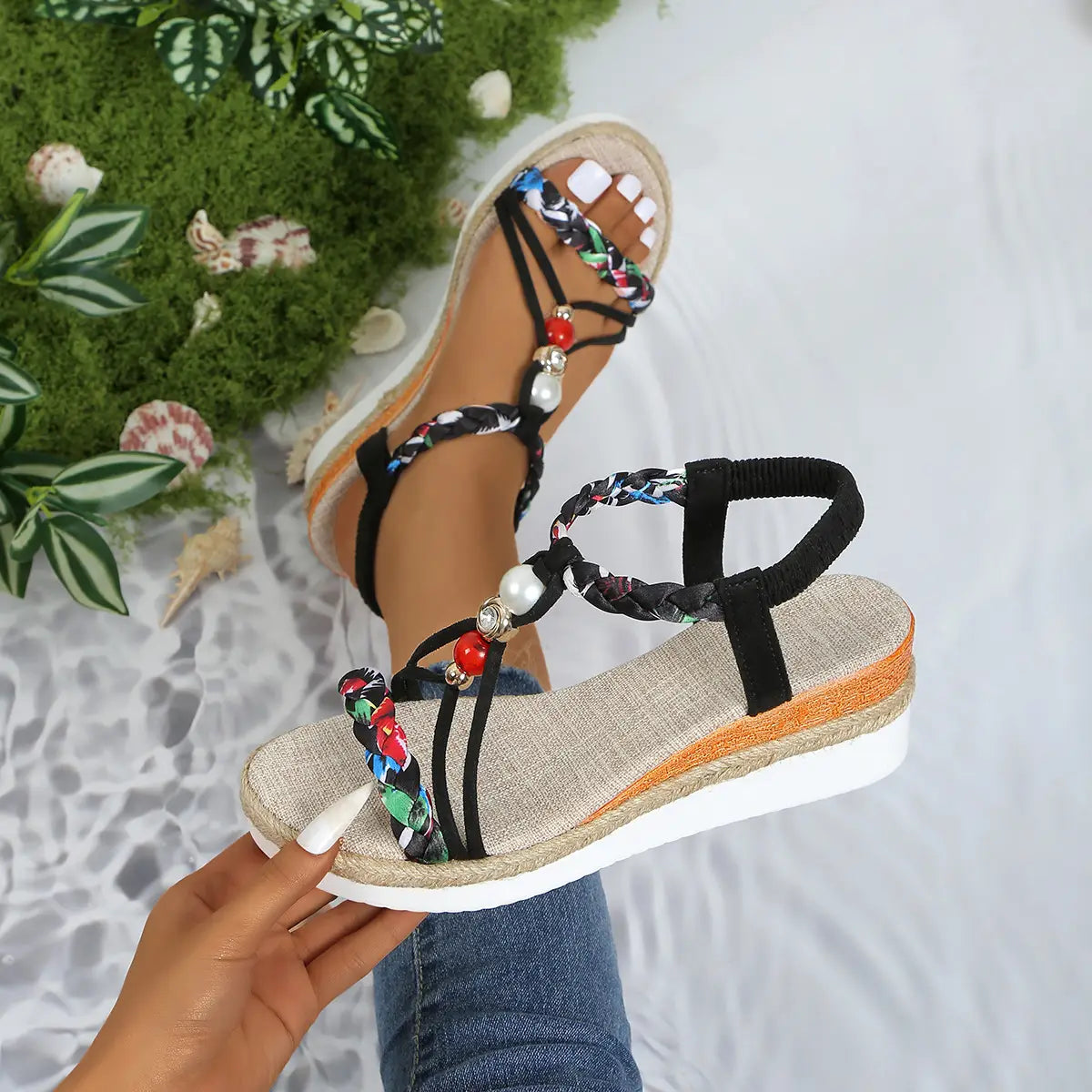 Sandalias tipo cuña para mujer con correas trenzadas negras y multicolor, con acentos de cuentas tipo perla y roja, y un tacón cuña espadrille tejida.