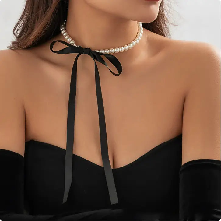 A delicate black satin ribbon tied into a bow at the center of an elegant string of small lustrous white pearls in a black satin and pearl ribbon choker bow jewelry set.