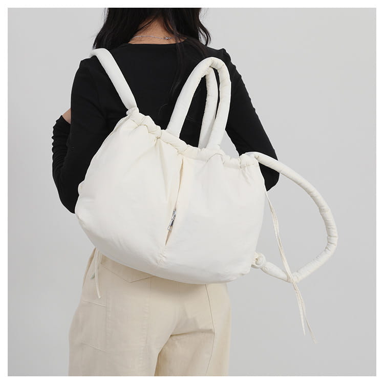 A plush white quilted puffer tote bag made of lightweight nylon featuring a soft puffy texture and padded looped handles.