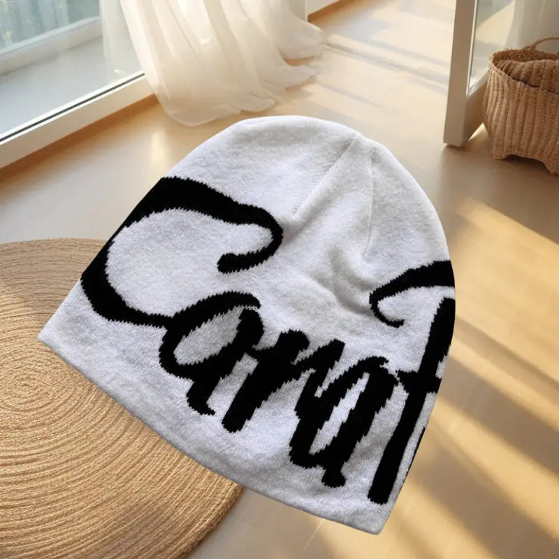 white knit beanie hat featuring bold black cursive embroidered lettering across the front made from soft knit material