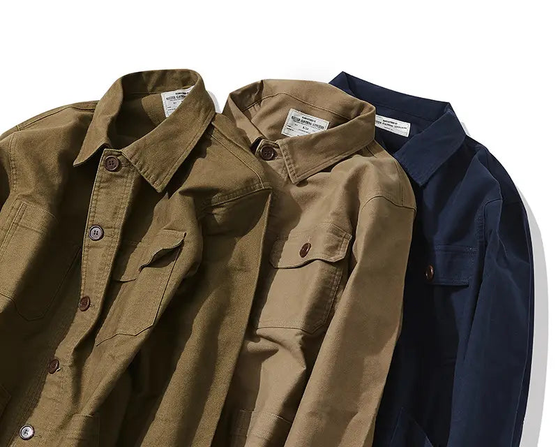 Three overlapping mens French workwear jackets in olive tan and navy blue featuring cotton material button closures and utility chest pockets.