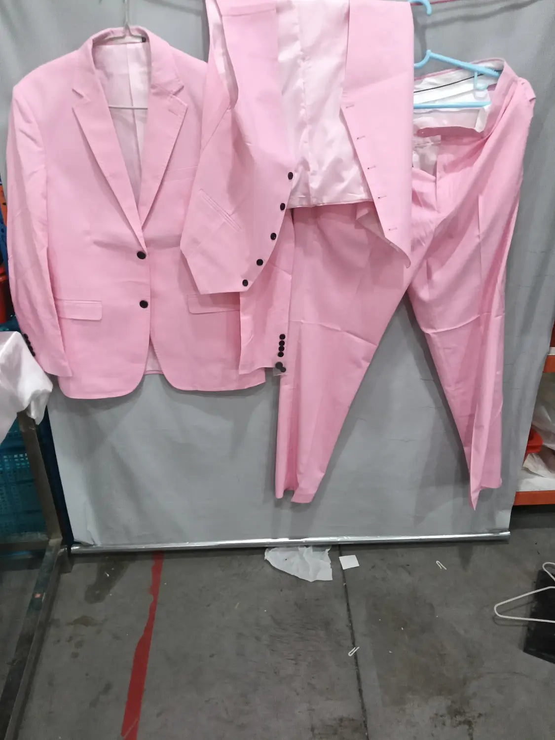 Un costume deux pièces en lin rose pour homme avec boutons noirs, suspendu sur des cintres, coupe slim, style décontracté, adapté à une tenue de marié, banquet