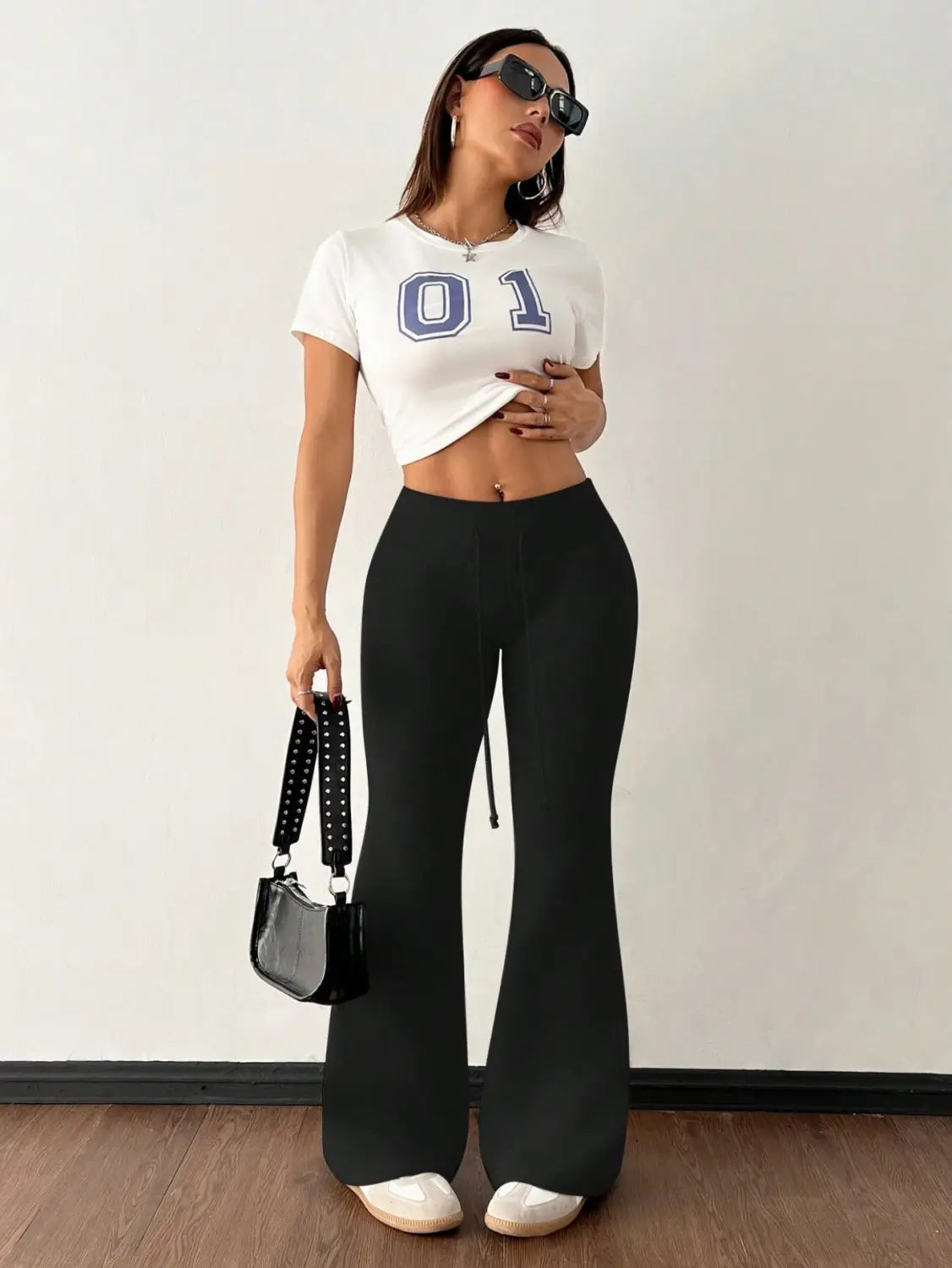 Black studded shoulder bag with glossy finish and adjustable strap paired with fleece lined high waist flared sweatpants.