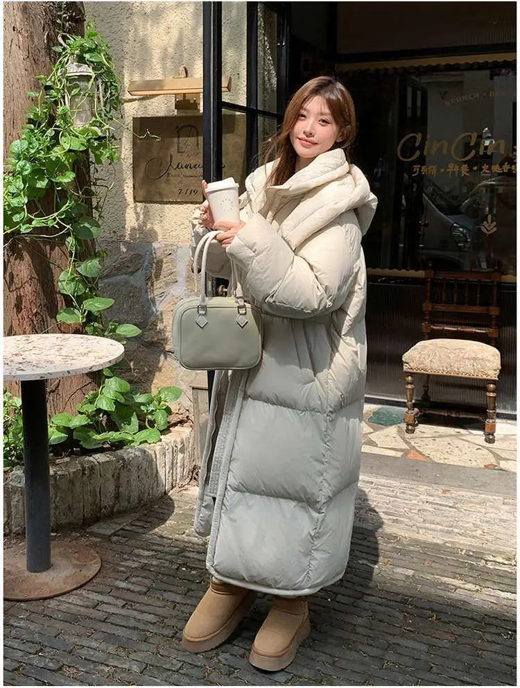 Un long manteau beige matelassé en duvet pour femmes, avec col haut et silhouette gonflée, adapté à la tenue d’hiver.