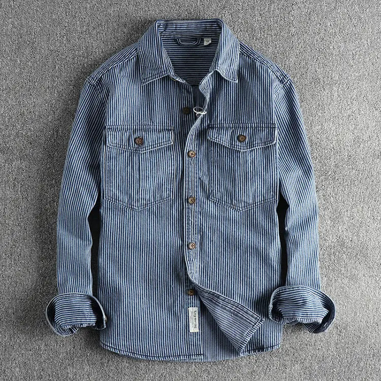 Striped denim shirt for men in blue and white vertical stripes with two chest pockets and brown buttons made of denim material.