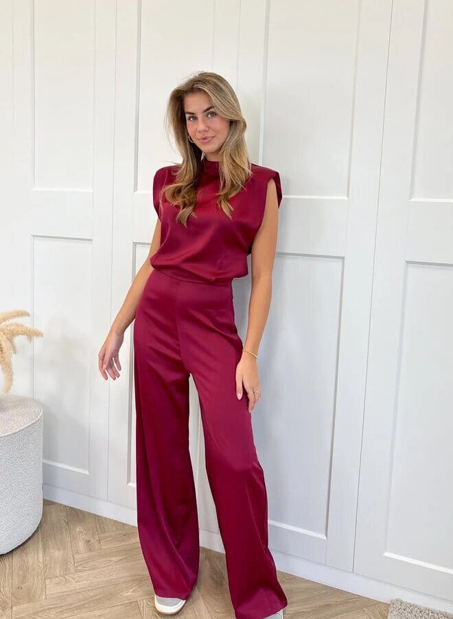 A sleek burgundy satin backless evening dress jumpsuit with a high neckline and wide-leg straight pants.
