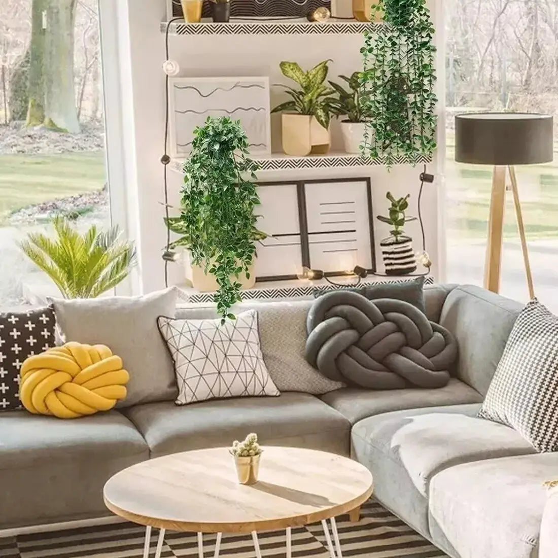 Gray sectional sofa featuring textured knit throw pillows and a yellow knotted cushion alongside a 3 pack of artificial hanging plants with fake trailing greenery.