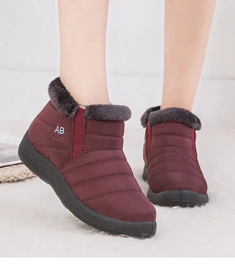 Botte d’hiver imperméable en neige bordeaux matelassée, avec bordure en fausse fourrure grise et semelle en caoutchouc noir, conçue pour offrir une chaleur moelleuse à la cheville et pour un usage en extérieur.