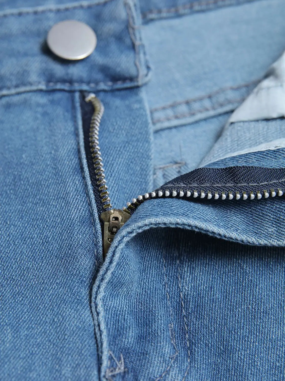 Men’s distressed slim fit stretch denim jeans in light blue featuring a metallic zipper and button closure.