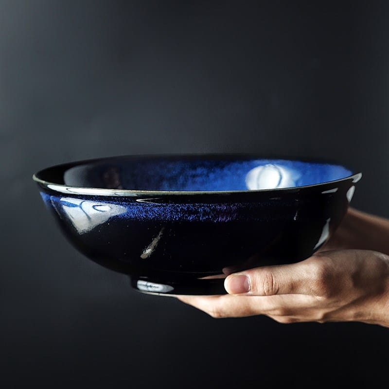 A deep cobalt blue ceramic ramen bowl with a glossy gradient glaze fading to black at the rim and base designed as an 8.5 inch cat eye blue noodle bowl.