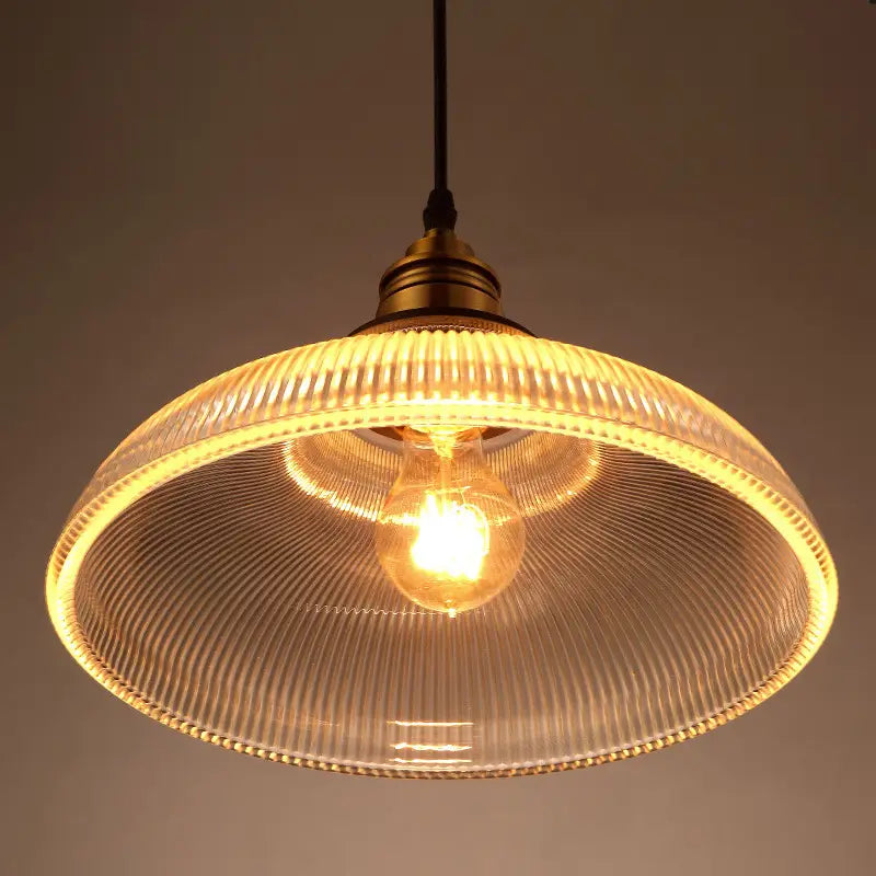 A warm-toned ribbed glass pendant light with a brass-finished metal fixture and an exposed bulb.