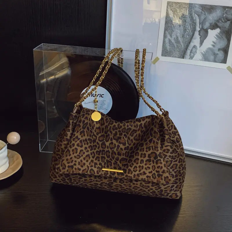 Leopard print crossbody bag with gold-tone chain straps and matching circular charm in leopard print pattern.