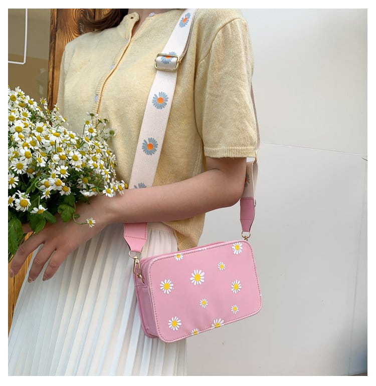 Pink daisy-patterned crossbody bag with a white strap featuring matching floral design and pink accents made of pu leather with a chain strap.