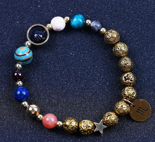 Zodiac volcanic stone beaded bracelet with gold charms featuring colorful textured gold-toned beads, vibrant blue and pink stones, metallic accents, star charm, and astrological symbol tag.