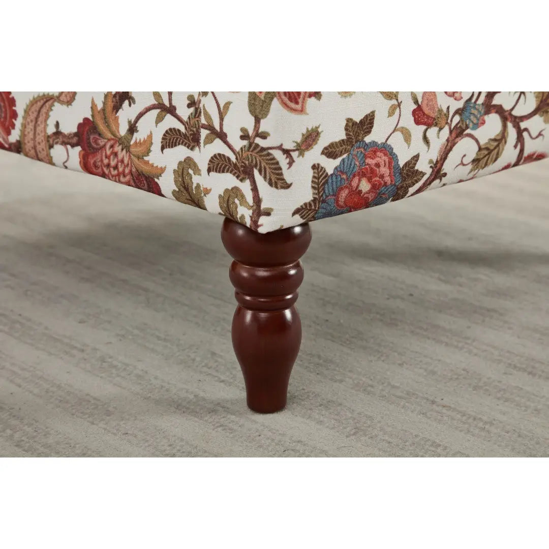 Una pata de madera oscura color marrón, con un diseño ornamentado torneado, que sostiene la silla tipo ala con respaldo capitoné floral con la tapicería de patas de madera retro