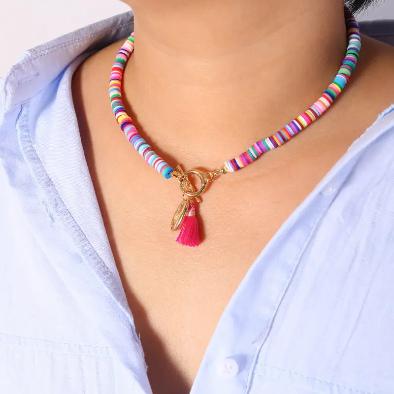 A vibrant multicolored beaded bohemian choker necklace featuring shell and tassel charms with a gold-toned toggle clasp and a pink tassel charm.