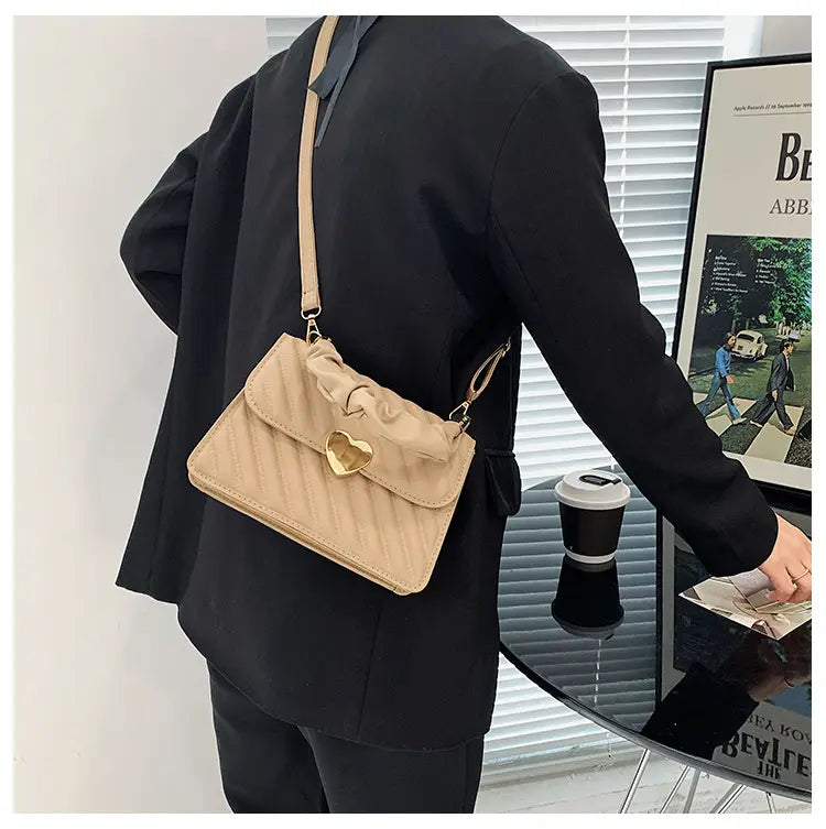 Beige quilted leather crossbody bag with gold heart-shaped clasp and ruffled flap featuring a ruched handle.