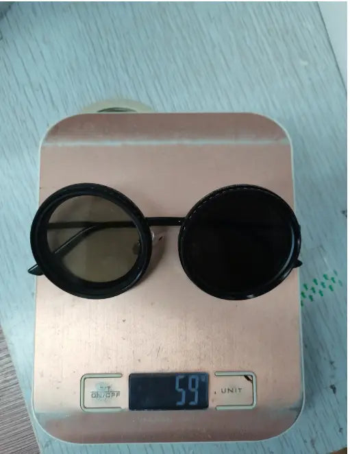 Lunettes de soleil rondes unisexes résistantes aux UV, à monture noire ronde et verres foncés, posées sur une balance numérique en or rose.