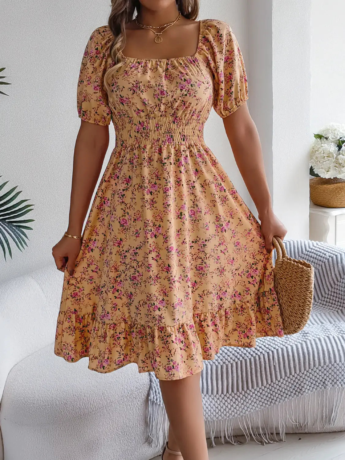 Une robe d’été florale pêche clair, avec manches courtes bouffantes et encolure carrée, présentant des détails à volants.