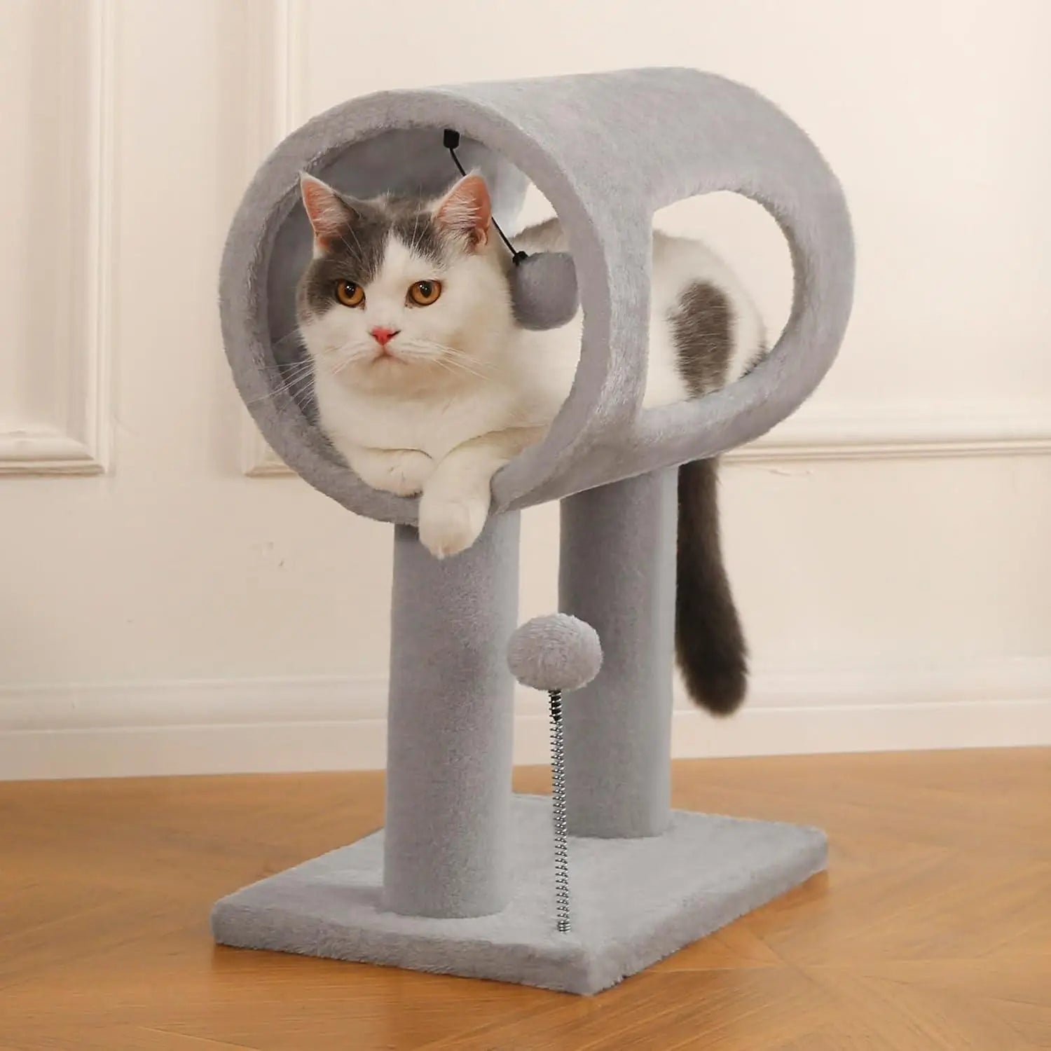 Gray cat tree with plush material featuring a circular tunnel and a dangling pom-pom toy for scratching and play.