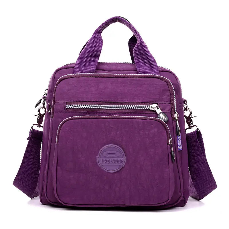 Purple nylon messenger bag with multiple zippers and a circular brand emblem designed as a crossbody canvas backpack.