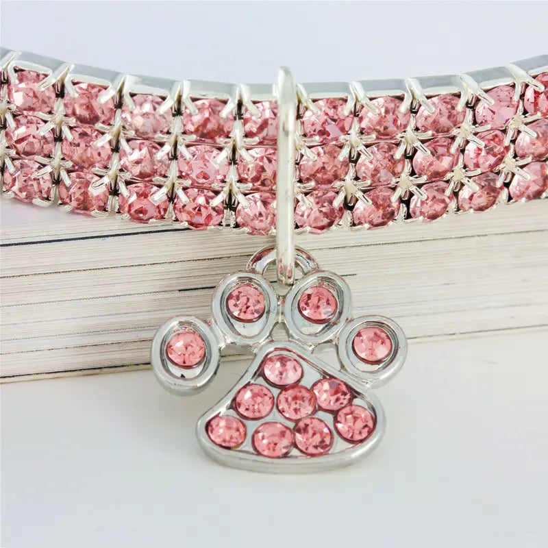 Un collier pour animal de compagnie en strass roses avec un charme assorti en forme de patte argentée, conçu pour les chiens.