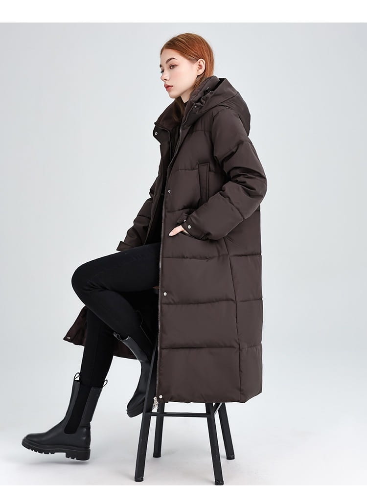 Manteau matelassé long à capuche pour femmes en brun foncé, coupe longue, avec capuche et fermeture boutonnée à l’avant.