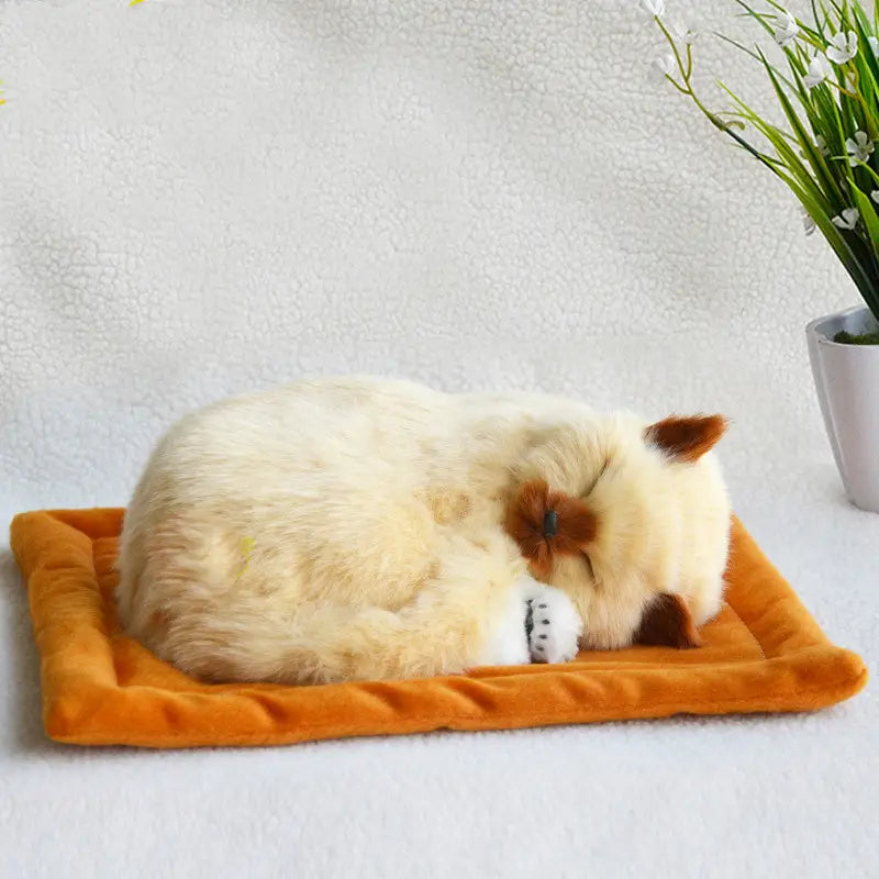 cream-colored plush cat figurine with brown accents on ears nose and paws resting on an orange velvet pet bed showcasing a realistic breathing feature.