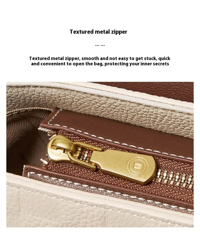 Goldtöniger strukturierter Metallschieber-Zipper mit elegantem, poliertem Zuggriff an einer zweifarbigen Webleder-Crossbody-Handtasche mit goldfarbenen Beschlägen.