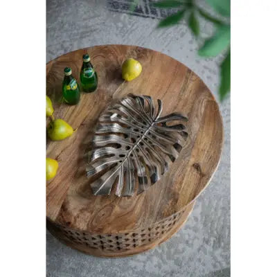 Silver monstera leaf-shaped serving tray with a metallic finish resting on a rustic wooden table from the gold monstera leaf wall decor and serving tray collection.
