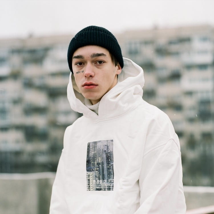 a white hoodie featuring a black and white cityscape graphic on the front paired with a dark gray ribbed wool beanie hat