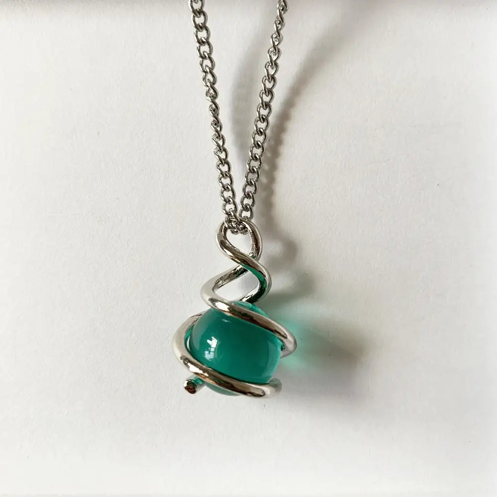 Collar de cadena de plata elegante y estilizado con un colgante esférico de vidrio brillante verde vibrante, rodeado por un diseño metálico retorcido y sofisticado en espiral.