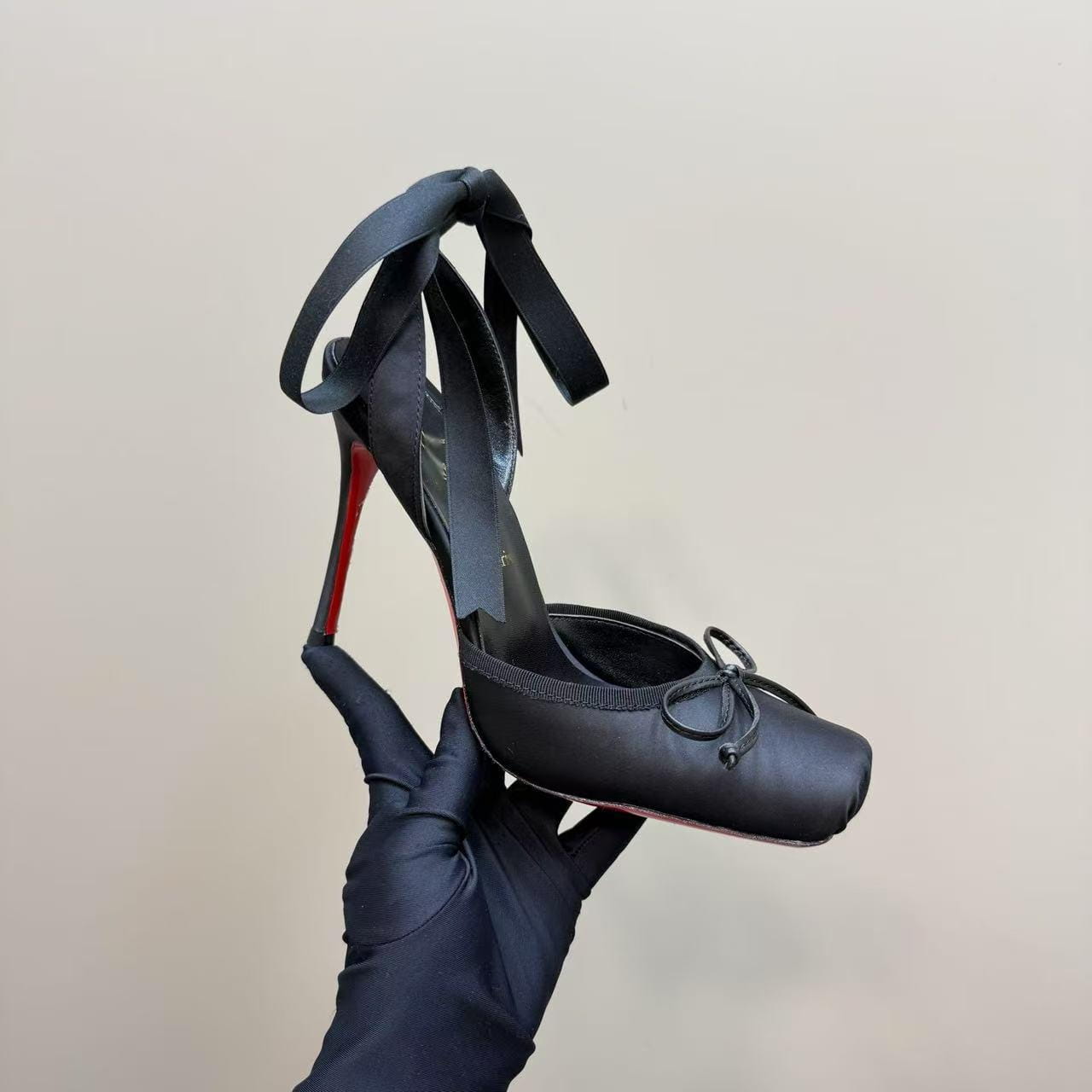 Black satin ballet flat with a red sole and ribbon tie featuring a leather sole and high heel design.