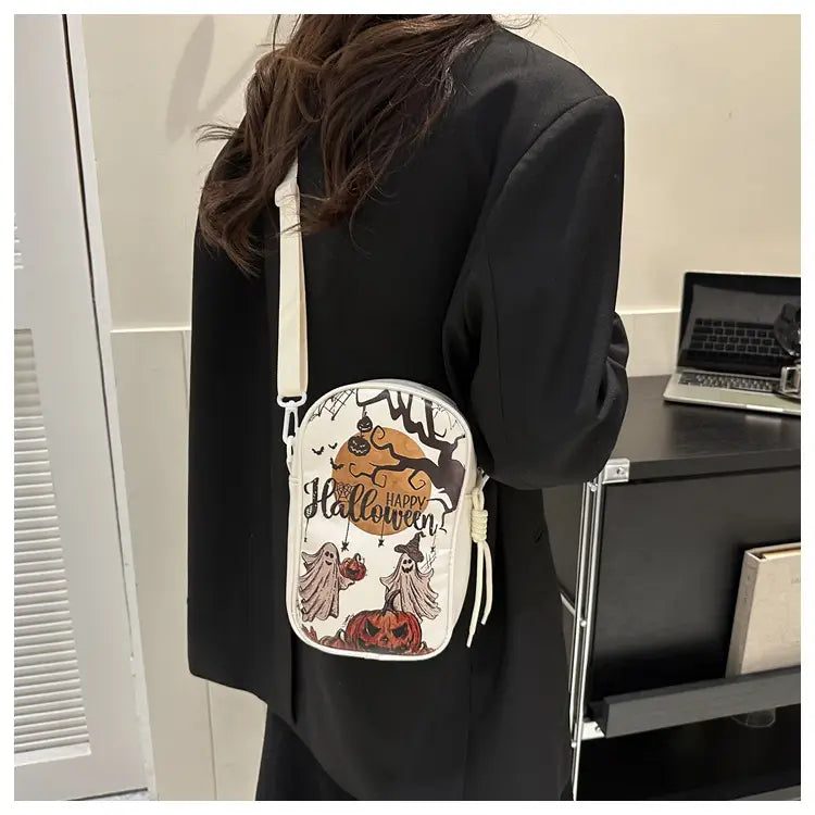 White embroidered Halloween floral and pumpkin crossbody bag featuring black and orange illustrations of ghosts pumpkins and a witch under the text happy Halloween.