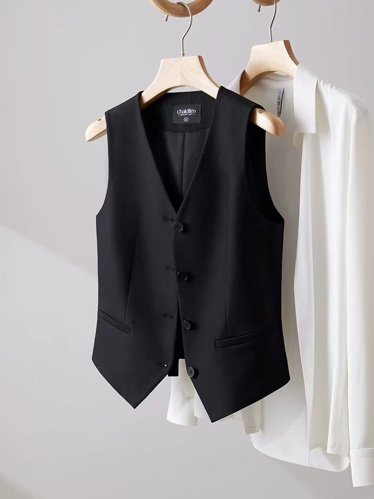 Schwarze Polyester-Damenweste mit maßgeschneiderter Passform, Chalton-Optik, fünf dunklen Knöpfen und zwei Vordertaschen, die an einem Holzkleiderbügel hängt.