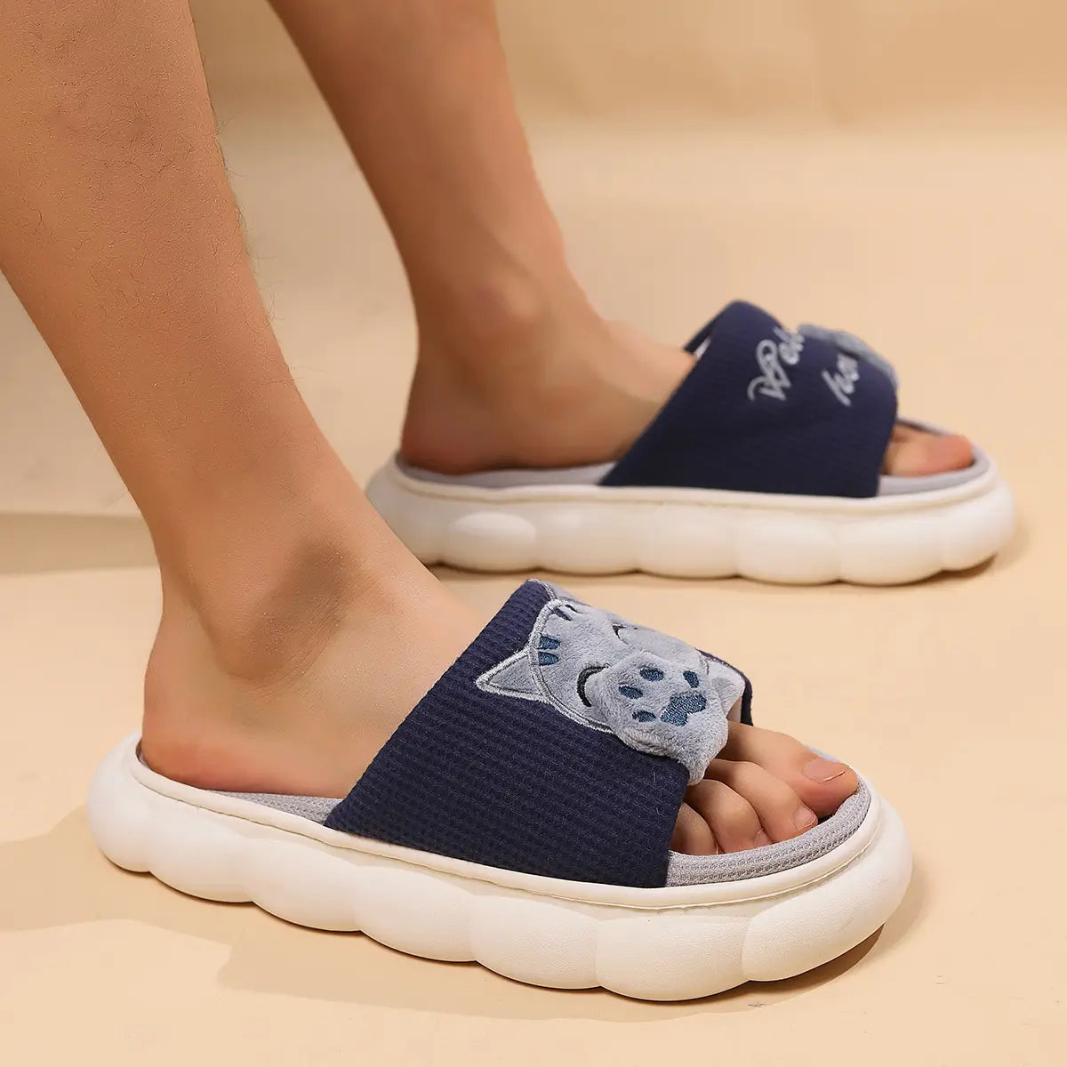 Navy blue slip-on sandals with a gray embroidered cat face on the strap and a white cushioned sole designed as unisex anti slip slide slippers.