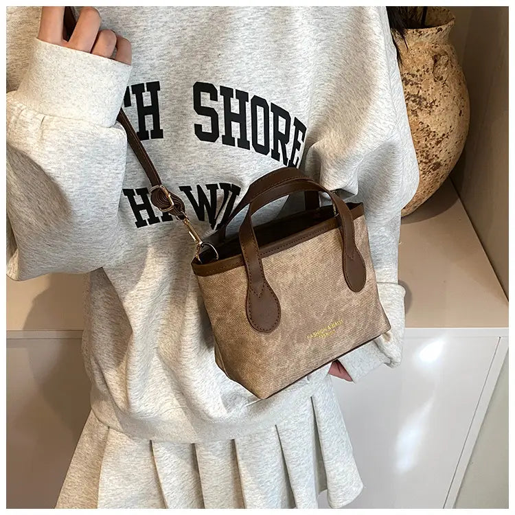 Beige canvas mini tote with brown leather handles and trim shown as a retro bucket bag textured canvas shoulder handbag.
